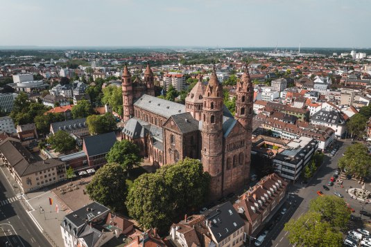 Luftaufnahme des Wormser Doms St. Peter, einer monumentalen Sandstein-Kathedrale mit vier T&uuml;rmen, eingebettet in die D&auml;cher und Stra&szlig;en der Stadt Worms., &copy; CC BY 4.0 MOCANOX GbR