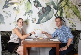 Paar stößt im Restaurant vor floraler Wanddekoration mit Weißwein an – Genuss in stilvollem Ambiente.